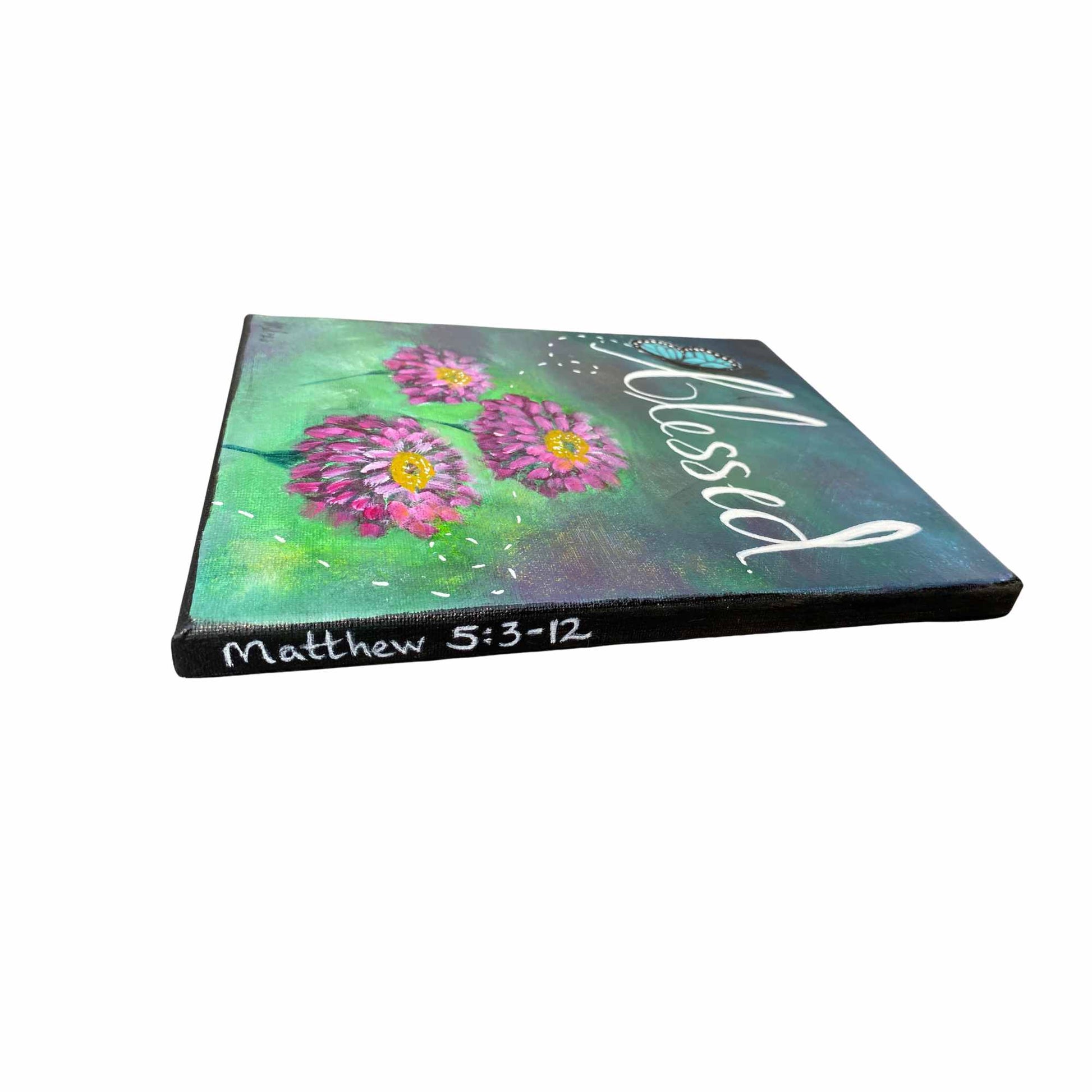 An 11x14" canvas painting shown at an angle, featuring three pink and purple zinnia flowers with yellow centers on a green and teal textured background. The word 'Blessed' is written in white script across the top, and 'Matthew 5:3-12' is written vertically on the side edge.