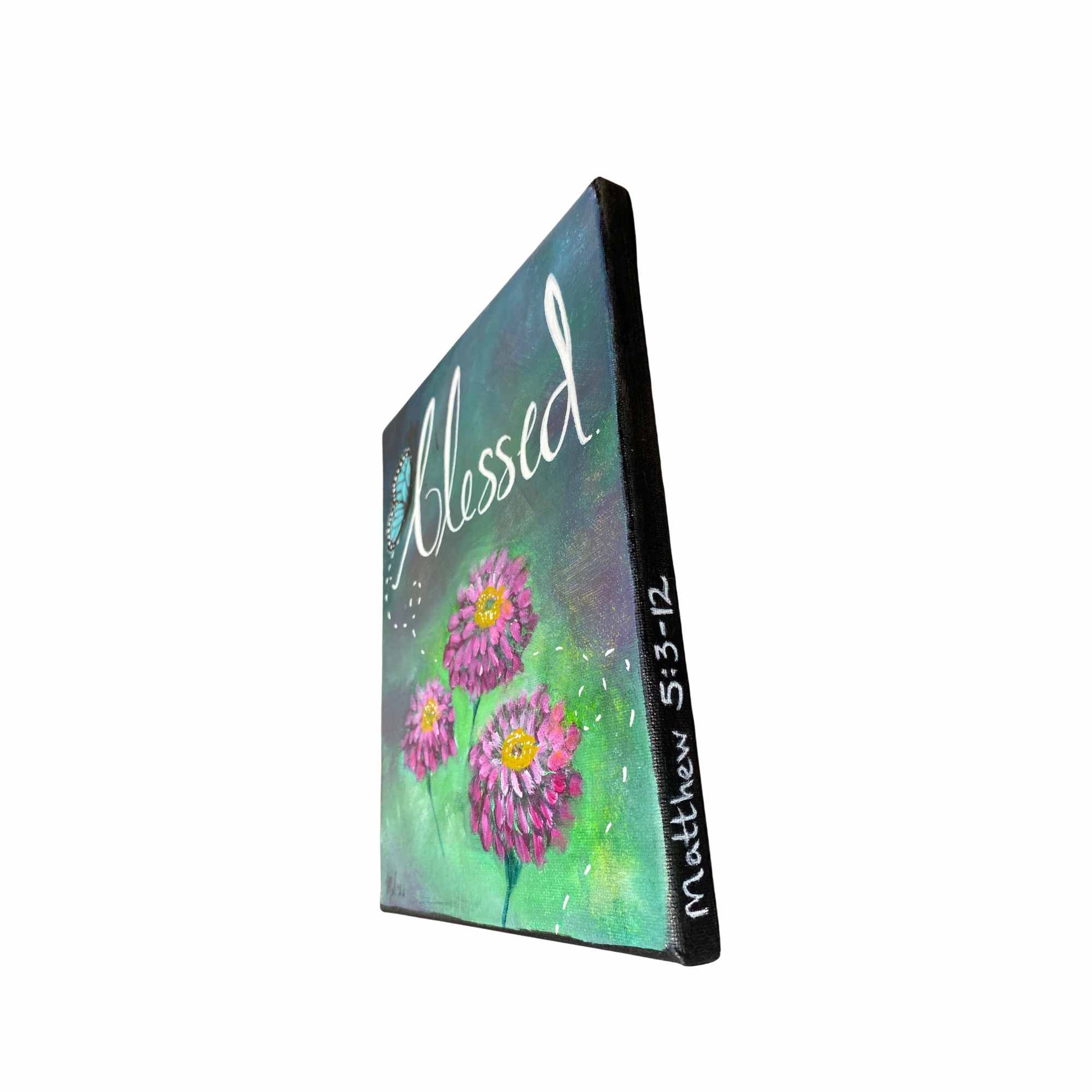 An 11x14" canvas painting shown at an angle, featuring three pink and purple zinnia flowers with yellow centers on a green and teal textured background. The word 'Blessed' is written in white script across the top, and 'Matthew 5:3-12' is written vertically on the side edge.