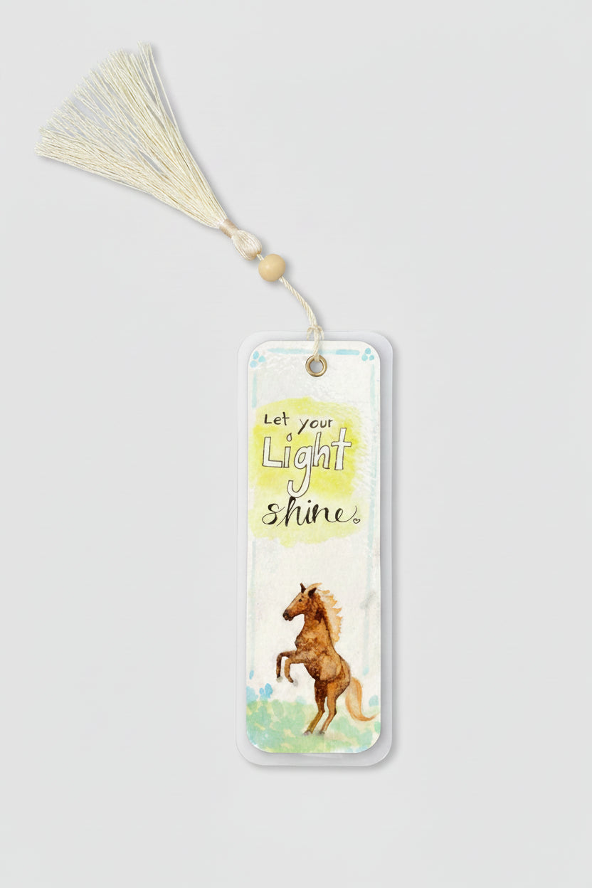 A rectangular laminated watercolor bookmark with a cream tassel and wooden bead, featuring the text 'Let your Light Shine' and an illustration of a brown horse.