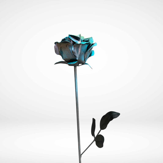 A single metal rose with metallic blue petals and dark leaves on a long stem, photographed against a clean light gray studio background.