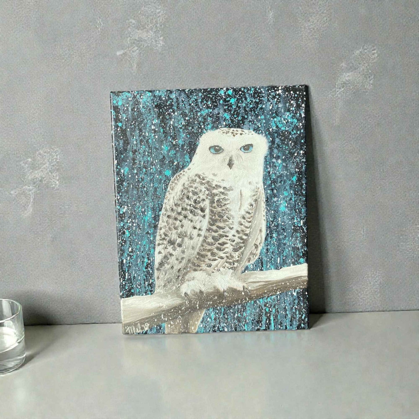 A 14x11" oil painting of a snowy owl perched on a branch, featuring a textured blue and black background, displayed on a gray surface against a gray wall.