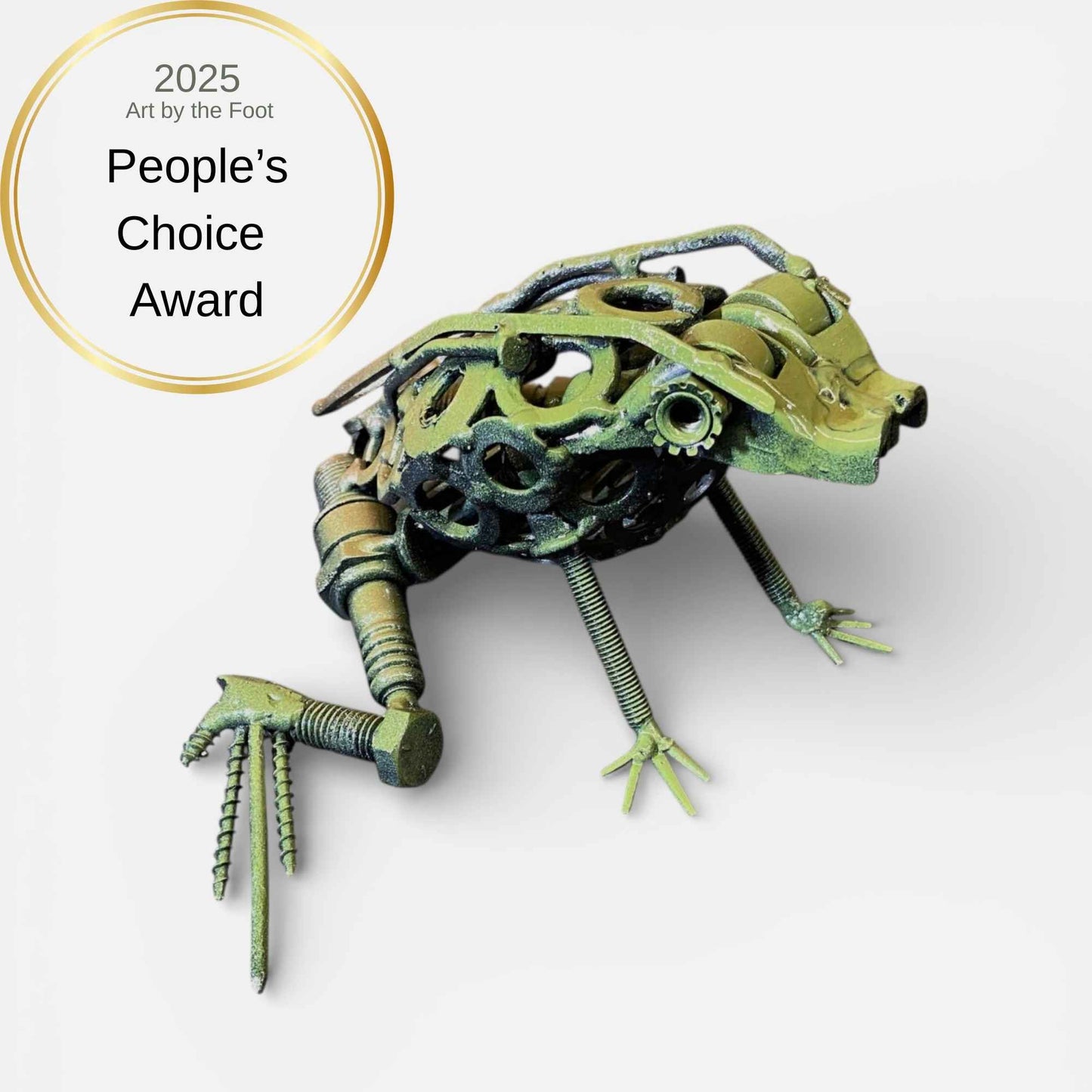 A sculptural frog made from metal parts, screws, gears, and bolts, shown on a light gray background with a gold circular award badge reading '2025 People's Choice Award' and 'Art by the Foot.' The product itself appears weathered in muted green and bronze tones.