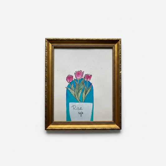 A framed art print featuring a white vase with pink tulips and the handwritten text 'Rise up' with a boho teal background, enclosed in an ornate gold frame.